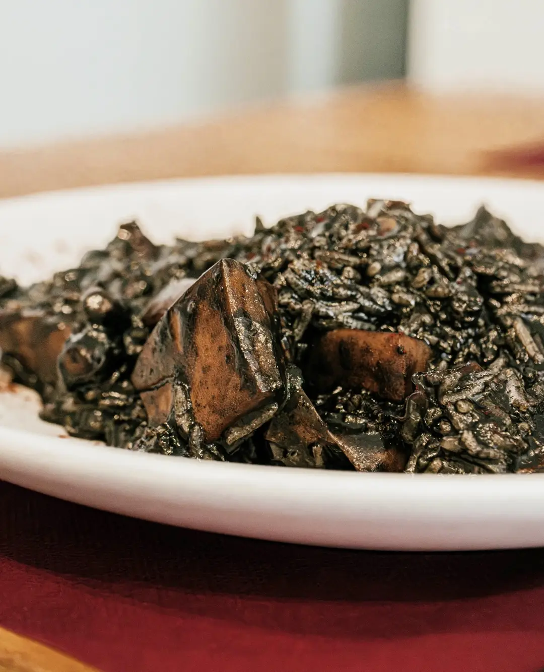 Arroz cremoso negro de choco de la ría en plato blanco sobre mantel burdeos