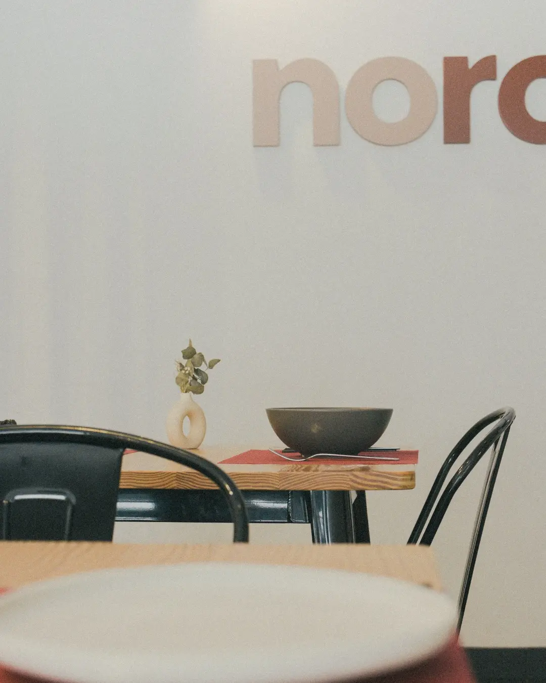 La sala de Noro, con el logotipo en la pared, mesas de pino y sillas negras